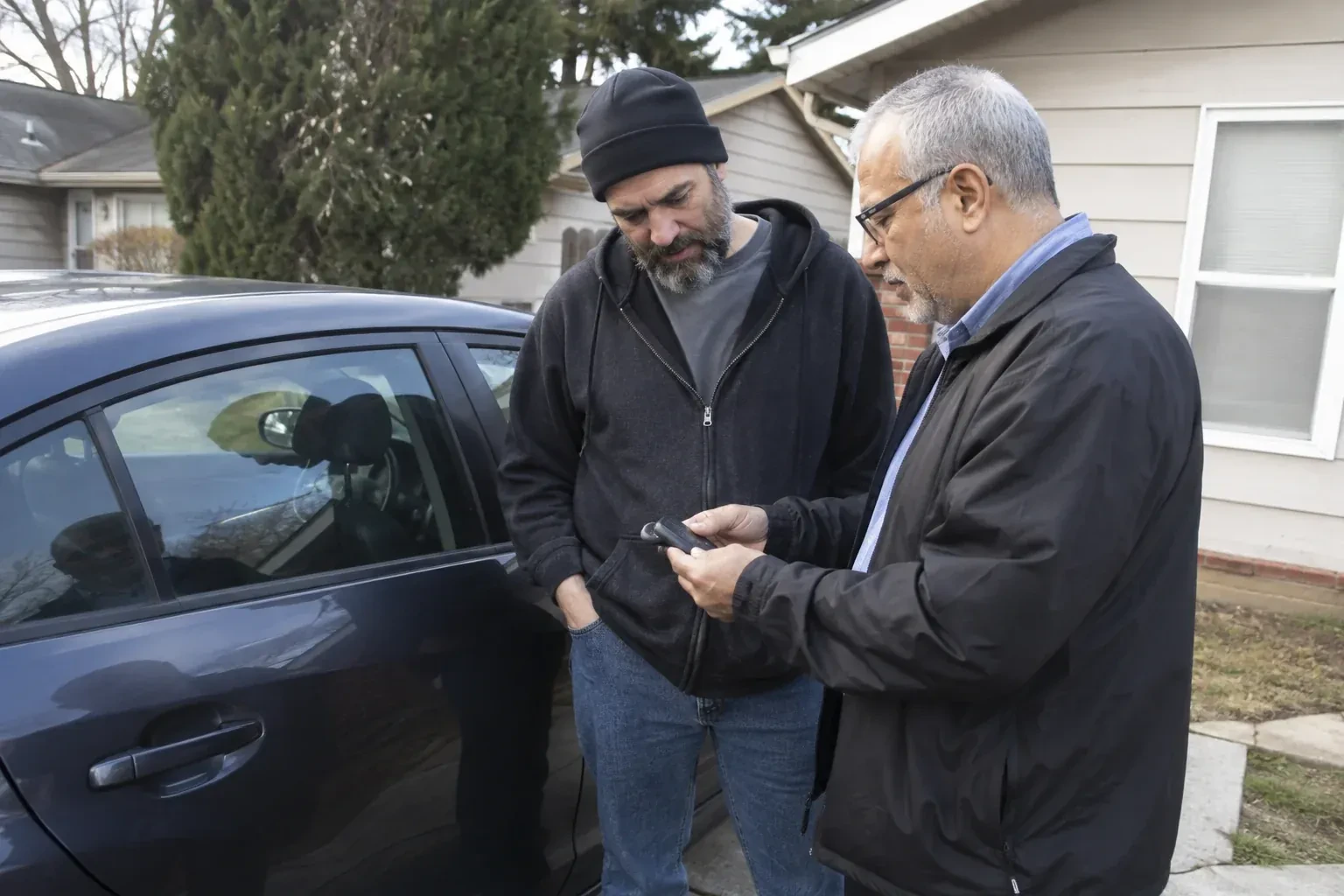 Two adults discussing a key fob beside a parked car. — Car Lockout Service, Kitchener