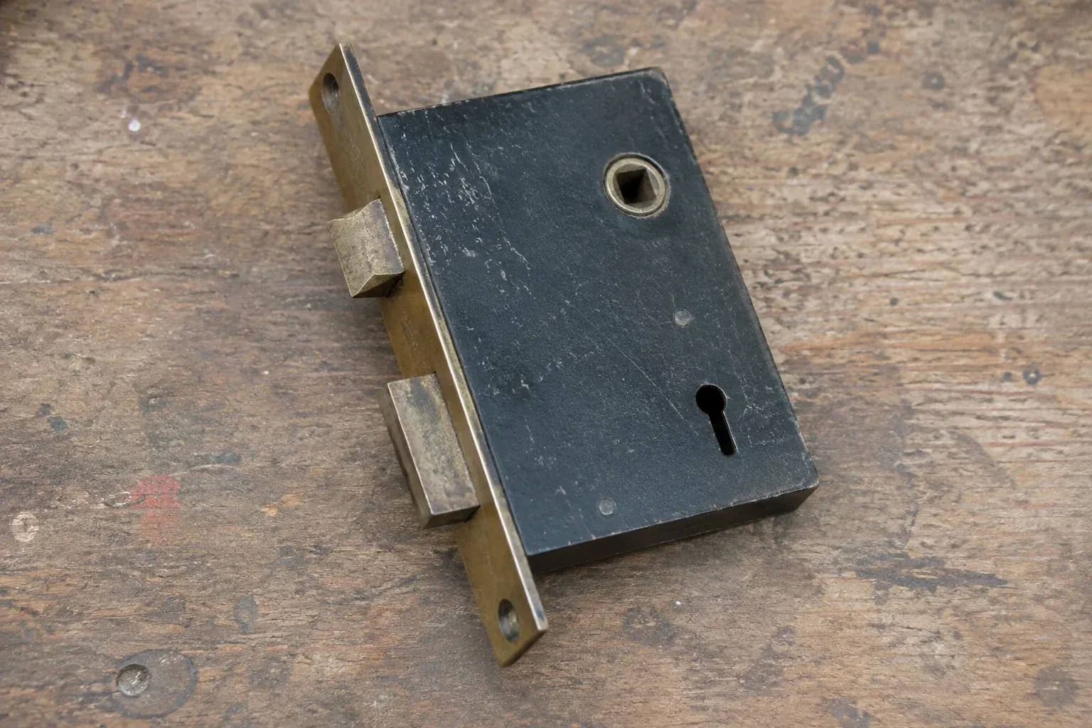 Closed mortise lock case with spindle opening, keyhole, latch and deadbolt on a wooden workbench. — Vintage Mortise Lock Service, Stanley Park