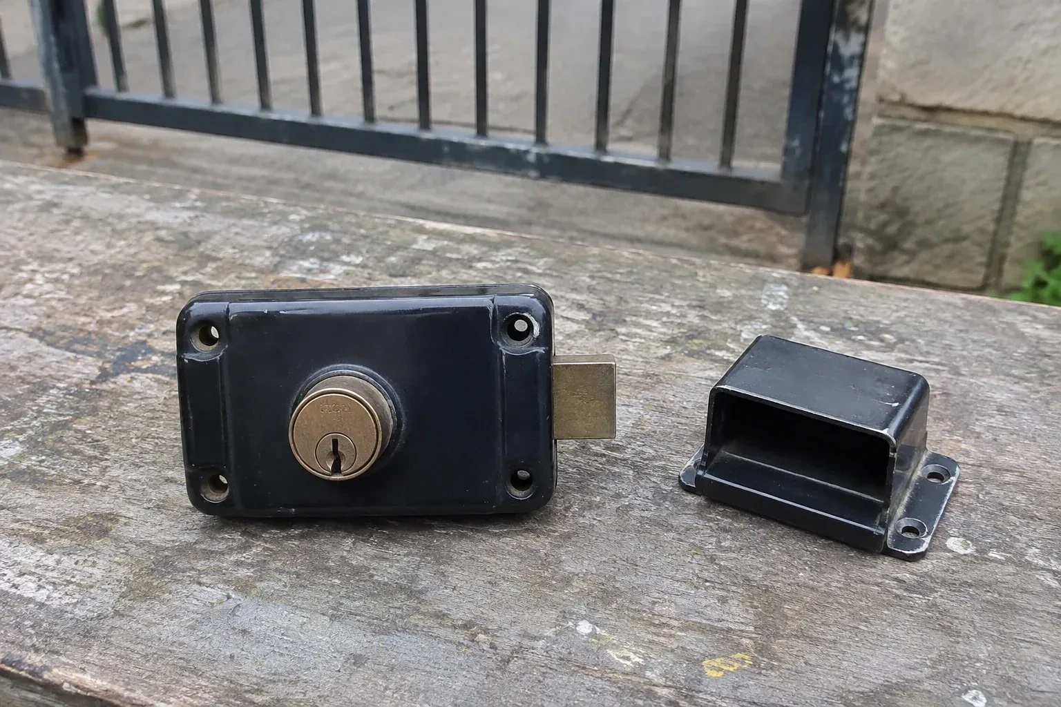 Detached rim gate lock and separate box keeper on an outdoor workbench. — Gate & Building Entry Locks, Rosemount